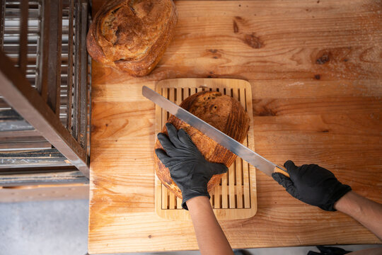 Artisan baker slicing crusty sourdough loaf on wood table