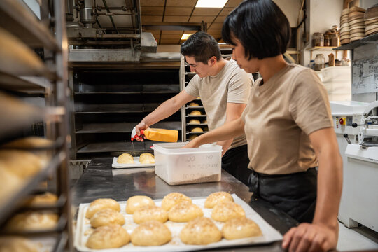 Artisan baker glazing bun trays in a busy bakery kitchen