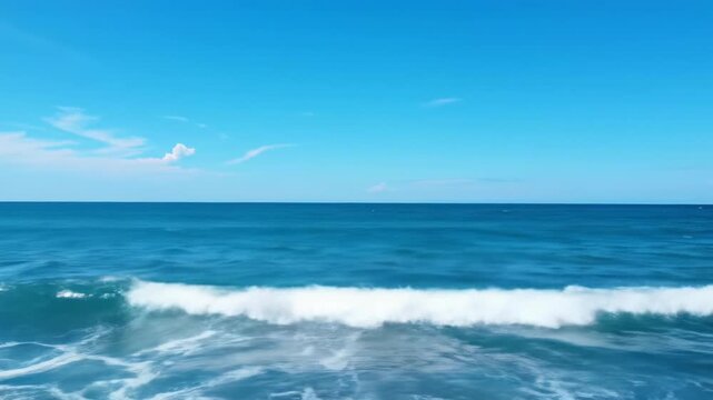 Expansive wide video of deep cerulean blue ocean waves with frothy white crests under a vivid azure sky with wispy clouds, razor-sharp horizon, slow push-in/pan. Deep depth of field. Concept of