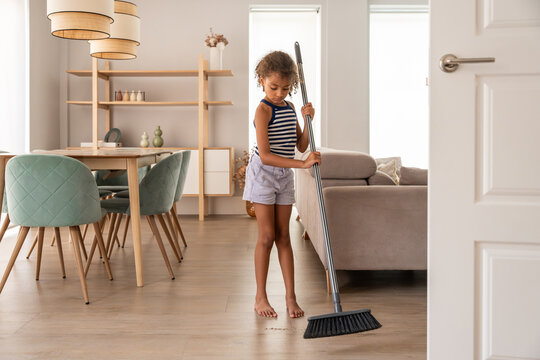 Child sweeping floor in bright modern living room at home