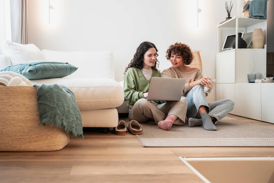 Two women using laptop together in cozy living room