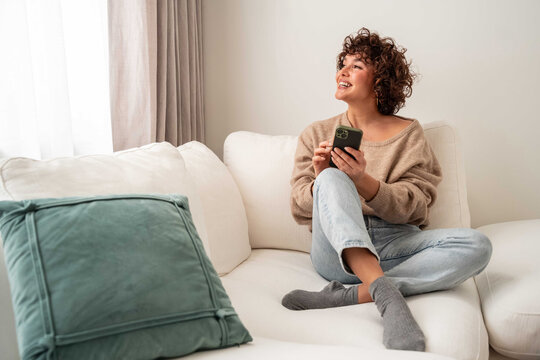 Woman relaxing on sofa using smartphone in bright living room