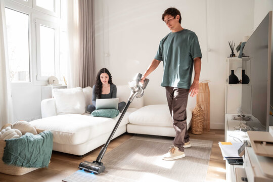 Man vacuuming living room while woman works on laptop