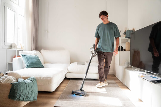 Man vacuuming rug in bright modern living room at home