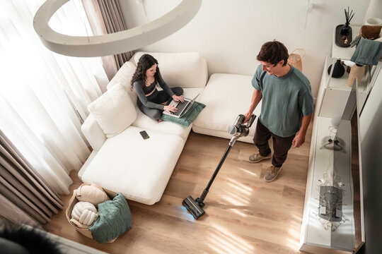 Couple at home: man vacuuming while woman works