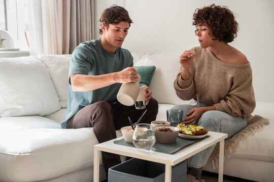 Couple sharing snack and drink on a cozy living room sofa