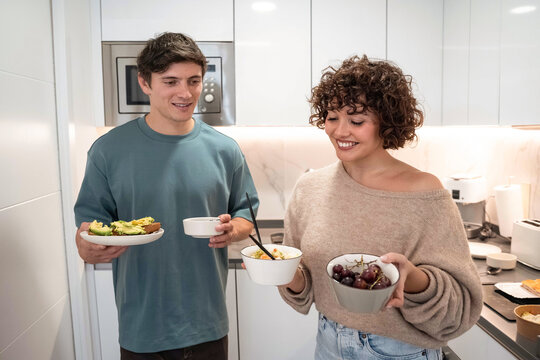 Young couple serving dinner and salad in modern kitchen