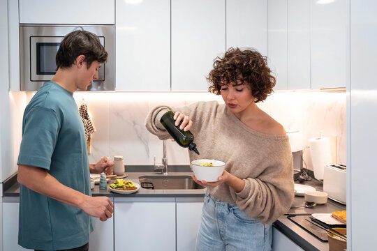 Couple preparing healthy salad with olive oil in kitchen