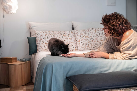 Woman feeding black cat on bed in cozy modern bedroom