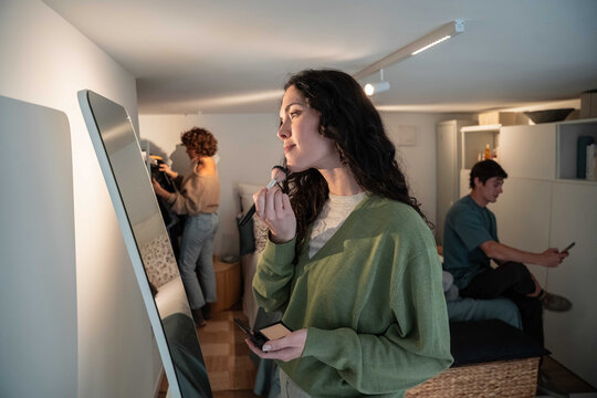 Woman applying makeup at mirror in shared apartment room