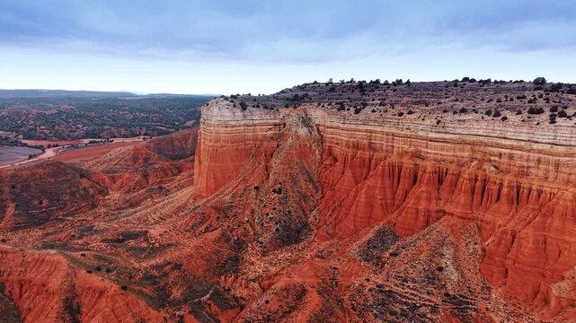 Drone view of red cliff escarpment and valley. Drone view of red clay escarpment, ravines, valley fields, shrubs, and overcast sky in Spain.