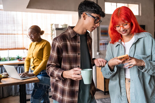 Young friends checking phone while coworker works in kitchen