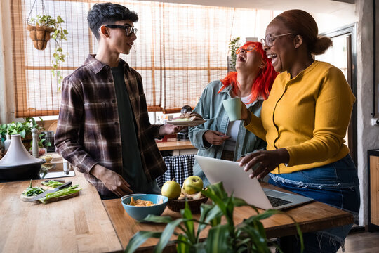 Diverse friends laughing with coffee and laptop in kitchen