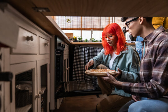 Couple placing homemade pizza into oven in cozy kitchen