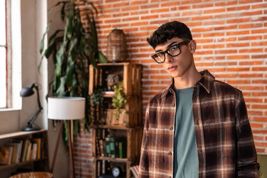 Young man in glasses posing in cozy loft with brick wall