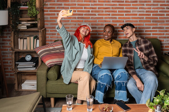 Friends taking selfie on sofa with laptop at home