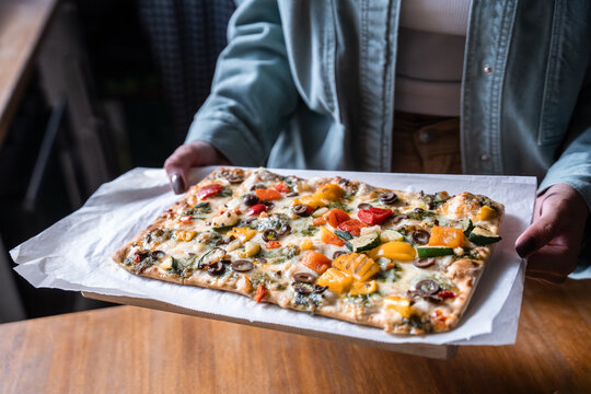 Person holding vegetable flatbread pizza on parchment paper