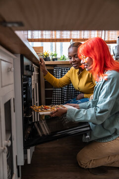 Two friends taking homemade pizza from oven in cozy kitchen