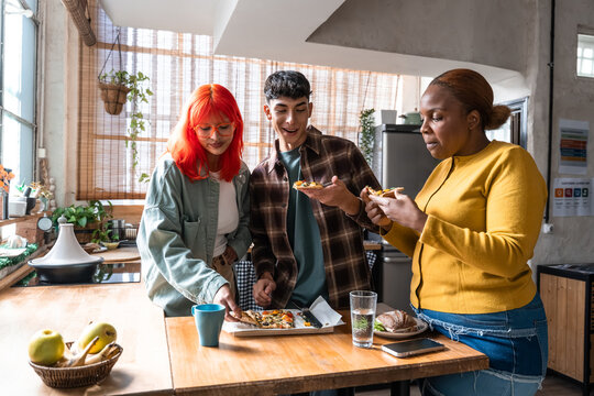 Friends sharing homemade pizza slices in cozy kitchen