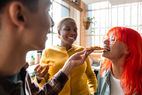 Friends laughing while sharing pizza slices in sunny kitchen