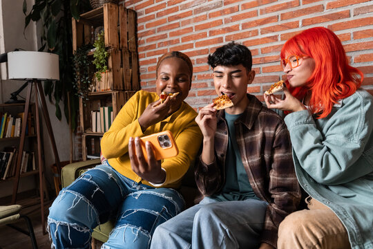 Friends eating pizza and taking selfie on a cozy sofa