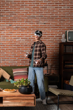 Young man playing VR game in living room with controller