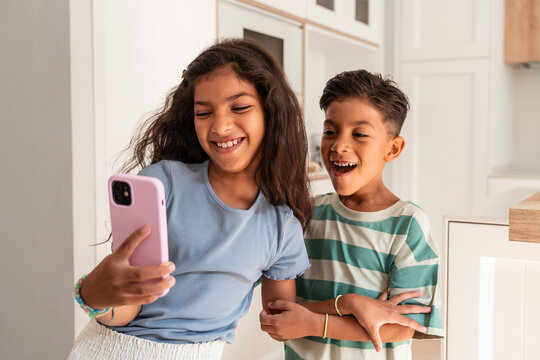 Hispanic siblings taking selfie on smartphone at home