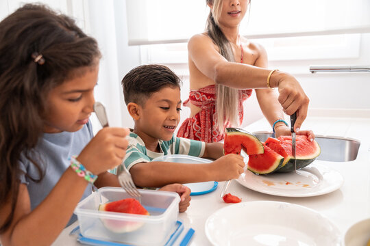 Hispanic family preparing watermelon snack in bright kitchen