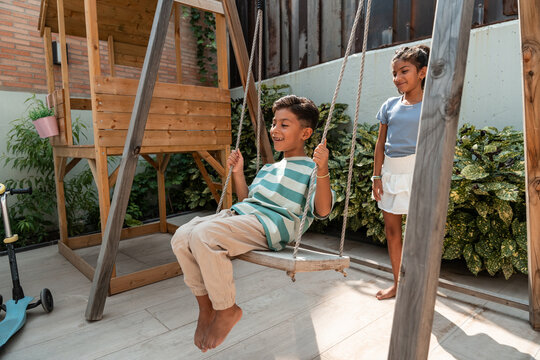 Hispanic children playing on backyard wooden swing set