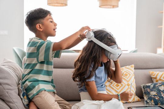 Hispanic siblings playing with VR headset at home