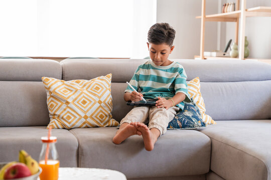 Hispanic boy drawing on digital tablet on living room sofa
