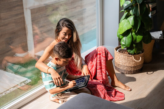 Hispanic mother and son bonding with tablet by window