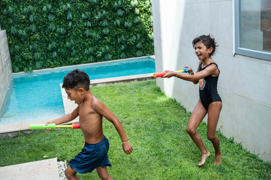 Hispanic siblings playing with water blasters by pool