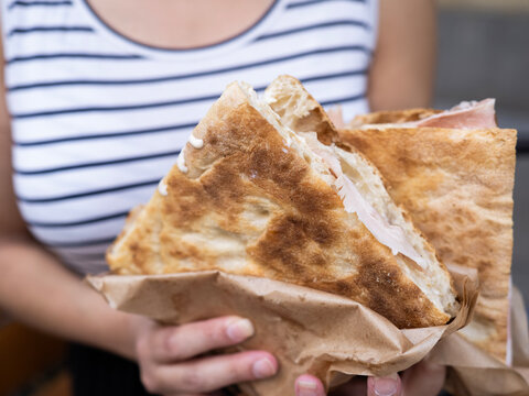 Person holding focaccia sandwich wrapped in brown paper