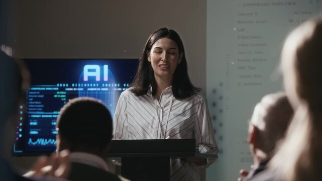 Rack focus over-the-shoulder shot of audience applauding middle-aged Caucasian woman taking podium, greeting new speaker during business conference dedicated to AI technology