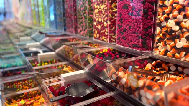 Abundant assortment of colorful, sugary gummies and jellies displayed in clear dispensers at a candy store, with scoops ready for a pick and mix selection of sweet confectionery