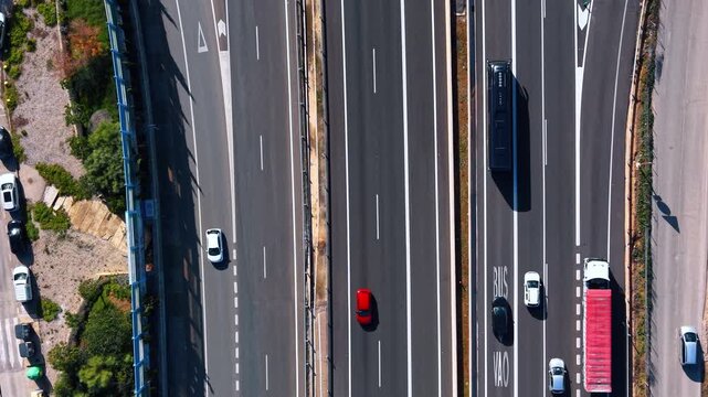 Top view of highway lanes with vehicles and bus. Vertical drone view of divided highway lanes with cars, bus lane markings, truck, shadows, and roadside parking.