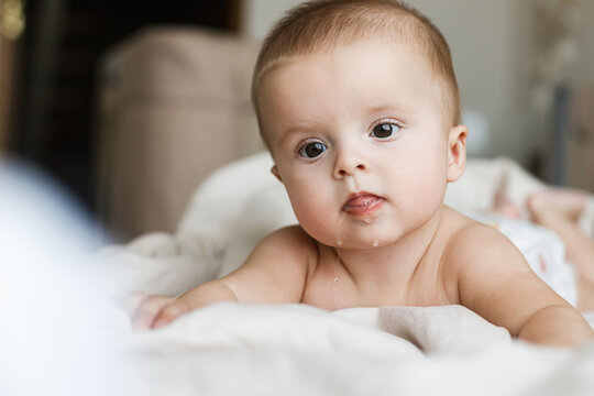 Adorable baby drooling in beige sheets in morning light. Time to sleep or wake up. Happy cute infant portrait on bed, space for text. Child sleep and childcare