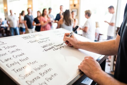 Hostess hands using a black marker to write a guest name on a restaurant dry erase waitlist board