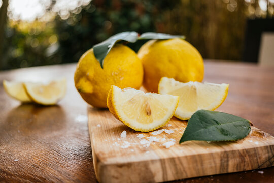 Fresh lemons and slices on wooden board in sunlight