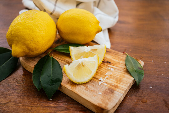 Fresh lemons with a sliced wedge on a wooden cutting board
