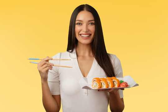 Portrait of woman holding sushi rolls on plate, enjoy eating traditional Japanese food and recommending delivery service, green background