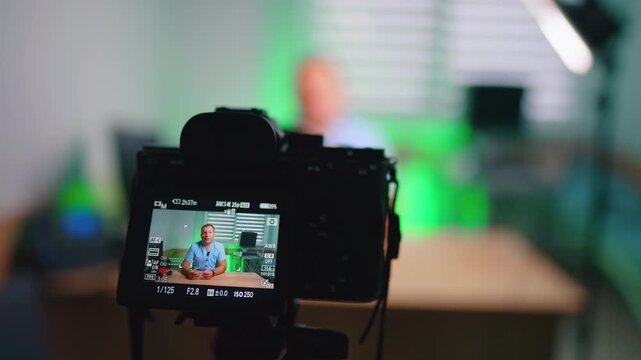 Close Camera View Of Doctor Recording Clinic Vlog. Close view of camera LCD showing doctor in blue scrubs, green clinic background, LED light.