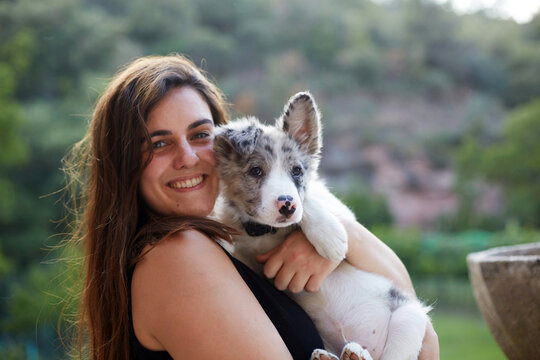 Smiling woman holding a border collie puppy outdoors