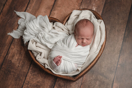 Sleeping newborn baby wrapped in blanket in heart basket