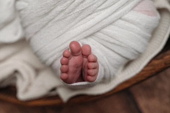 Sleeping newborn wrapped in white blanket with tiny feet