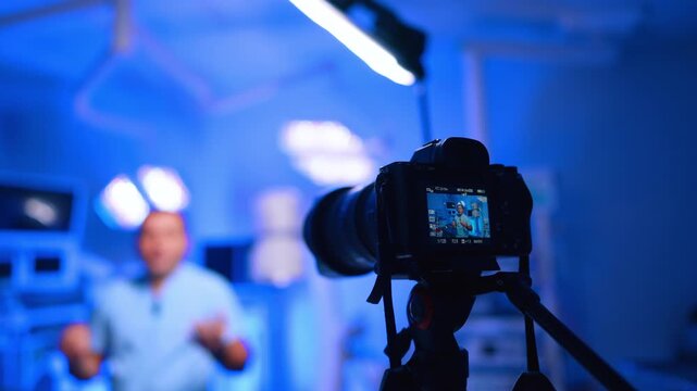 Camera Records Doctor Vlog With Blue Clinic Background. Close camera records blurred doctor in blue clinic, screen display, shallow depth of field and LED light.