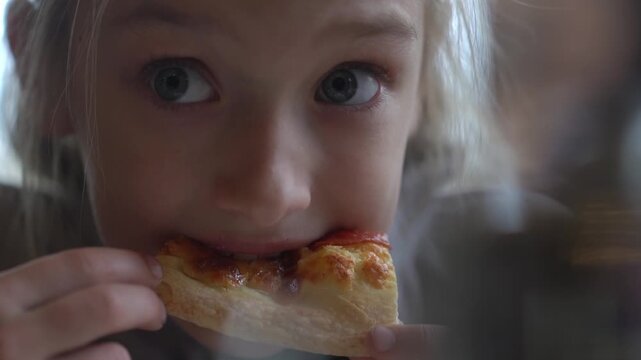A cute girl eats pizza with her hands in a cafe. A hungry child munches on fast food. A snack at a cafe. High quality FullHD footage