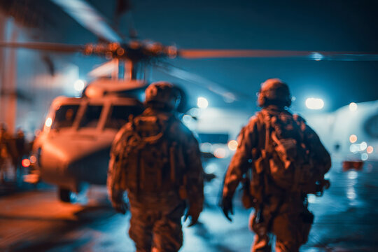 Two soldiers walking towards a helicopter on a wet runway at night with blurred background featuring bright lights and aviation equipment