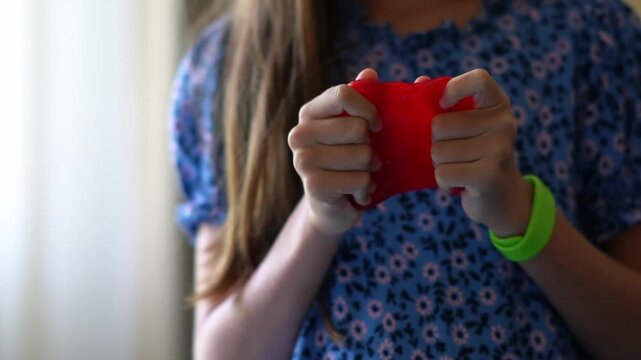 A child plays with homemade red slime. A fun sensory activity, fine motor development, and a concept for educational content, toy stores, home child development, and resort entertainment. 